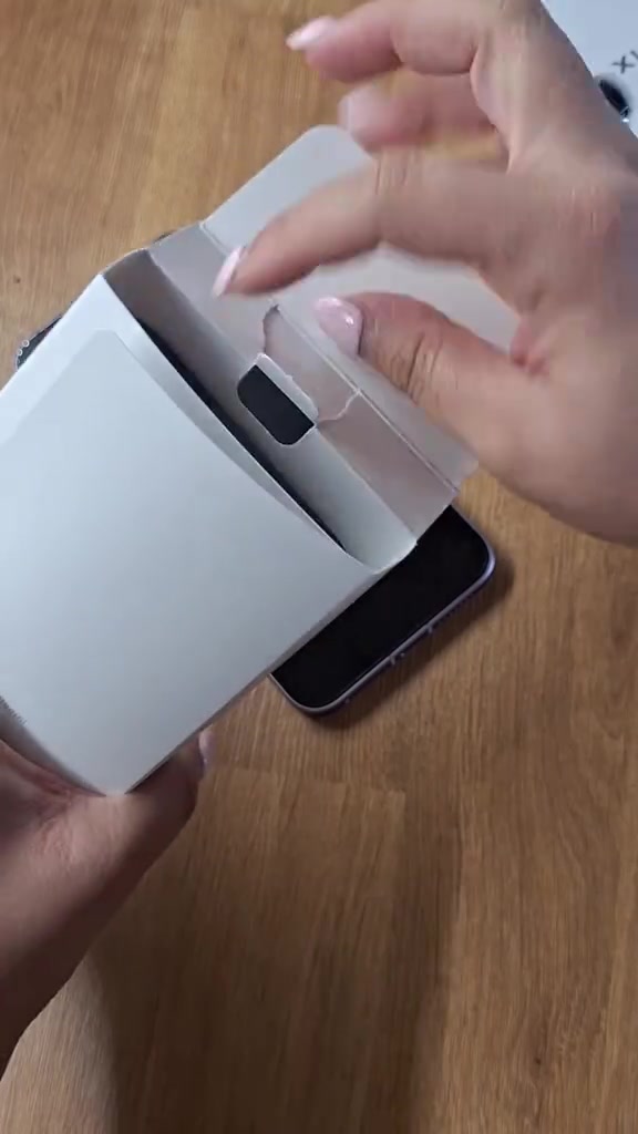 Tangan membuka kompartmen dalam kotak Xiaomi 17T Pro dengan telefon terbaring atas meja kayu di sebelah