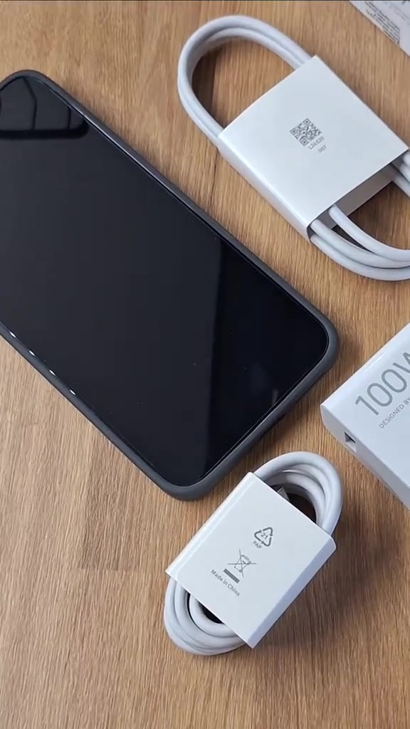 Xiaomi 17T Pro bercase kelabu terbaring atas meja kayu bersama gulungan kabel putih dan kotak adapter bertulis 100W