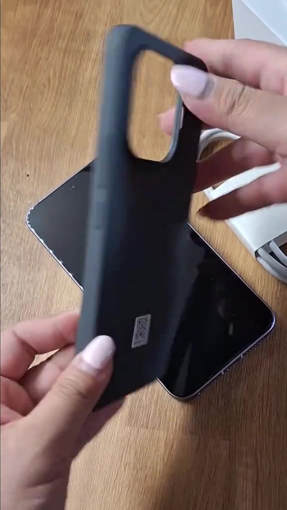 Tangan memegang case hitam bawaan Xiaomi 17T Pro di atas badan telefon yang terbaring, kabel putih kelihatan di sebelah