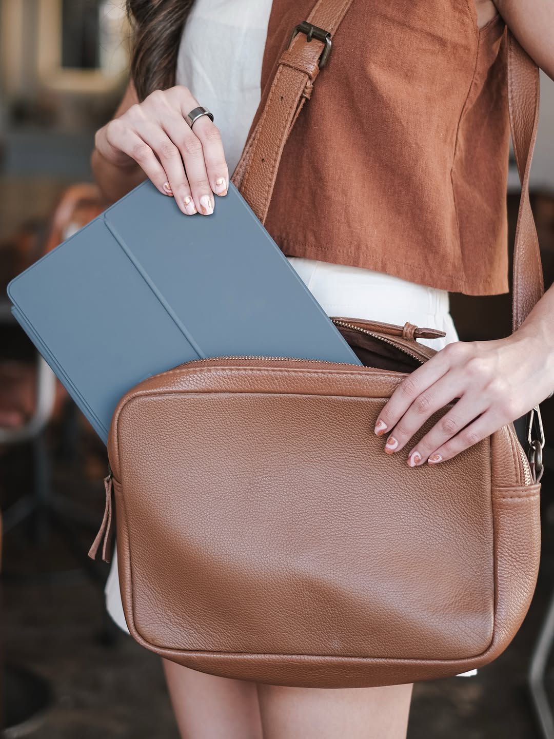 Tablet dengan folio kelabu dimasukkan ke dalam beg galas kulit coklat