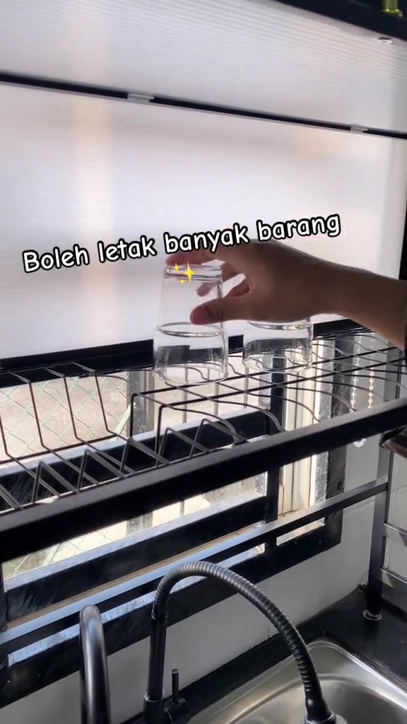 Tangan meletakkan gelas terbalik di atas rak jaring pinggan yang berdiri atas sinki stainless steel