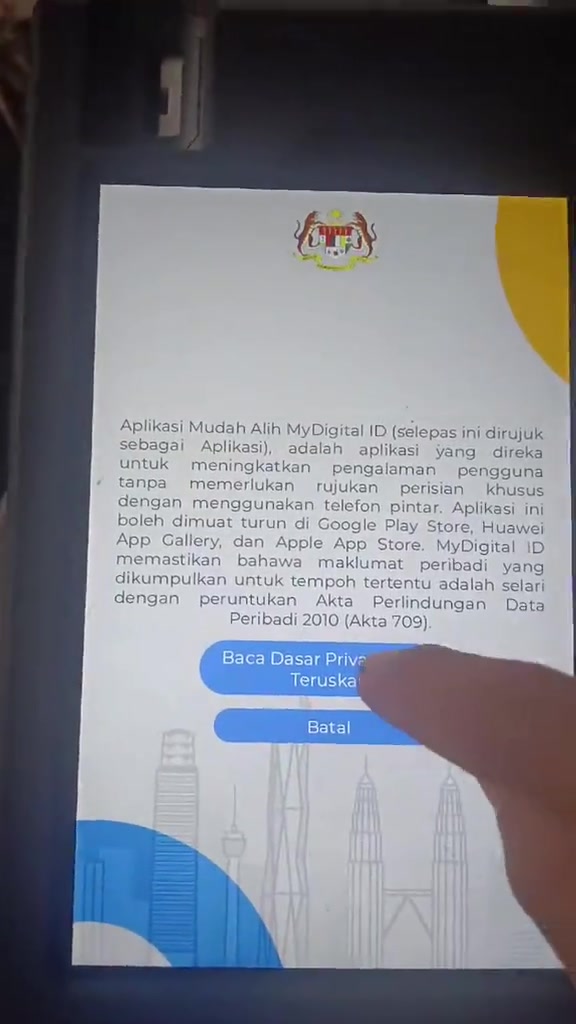 Skrin kiosk MyDigital ID paparan dasar privasi dengan butang Teruskan dan Batal serta jari menekan skrin