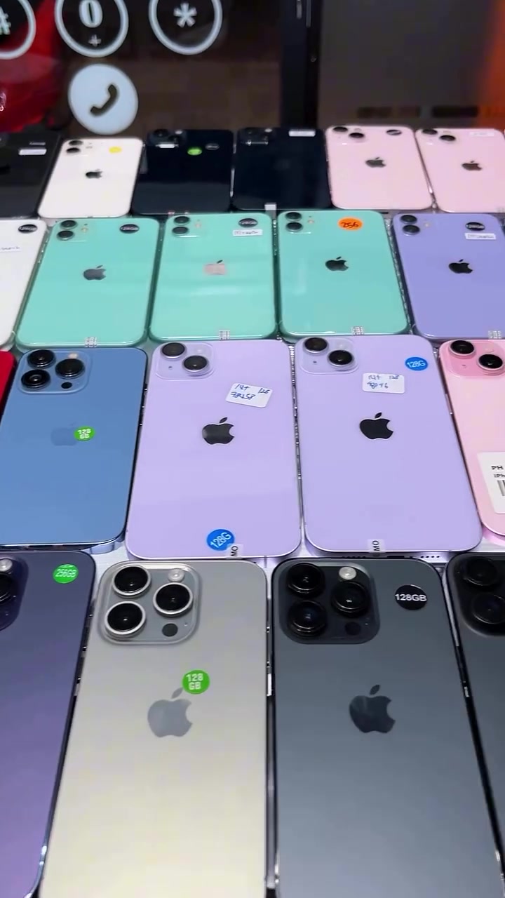 Puluhan iPhone secondhand pelbagai warna tersusun berderet dengan pelekat storage di atas meja kedai