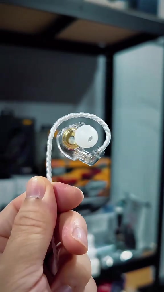 Earphone in-ear monitor (IEM) badan lutsinar dengan kabel berpilin dipegang pada tangan