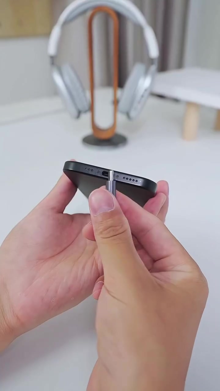 Tangan mencucuk penyambung USB-C ke port bawah telefon dengan headphone di latar belakang