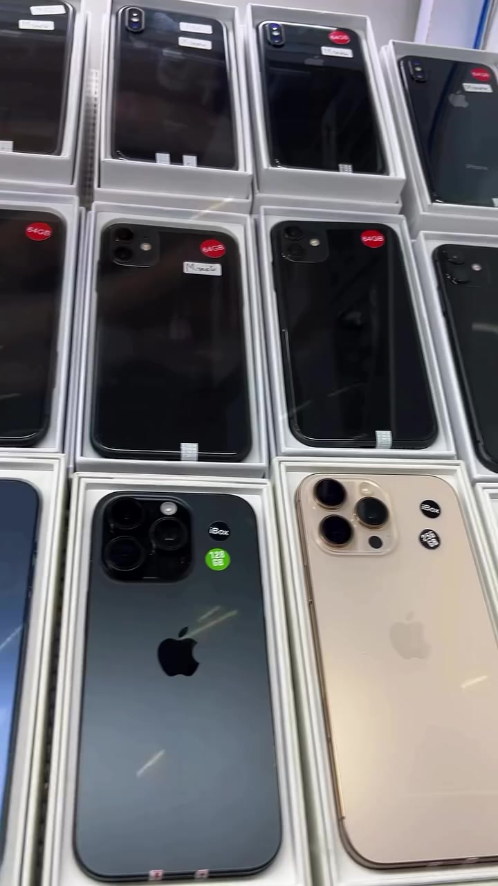 Deretan iPhone secondhand dalam tray kotak putih dengan pelekat stok kecil di sebuah kedai telefon