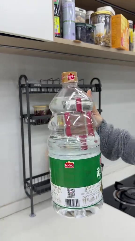 Tangan memegang botol air besar di depan rak dinding lekat sebagai ujian beban pelekat