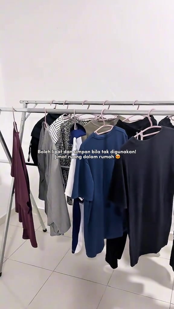 Ampaian lipat dalam rumah dengan beberapa helai baju bergantung pada penyangkut berwarna merah jambu