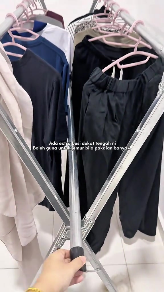 Ampaian lipat stainless dalam rumah dengan baju bergantung rapat pada penyangkut, sebelah tangan sedang laras bar tengah