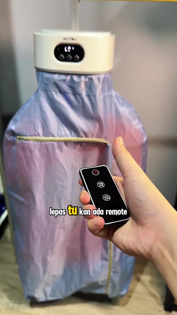 Unit portable dryer berwarna putih dengan paparan digital, sebelah tangan memegang remote hitam di hadapan kanvas biru