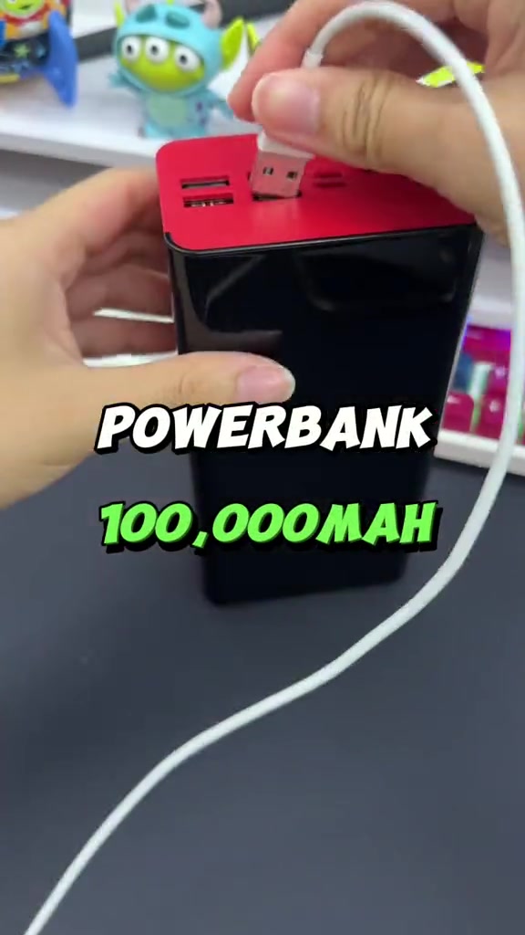 Power bank menara hitam bertop merah dengan kabel USB dicucuk, bertulis 100,000mAh dalam video viral