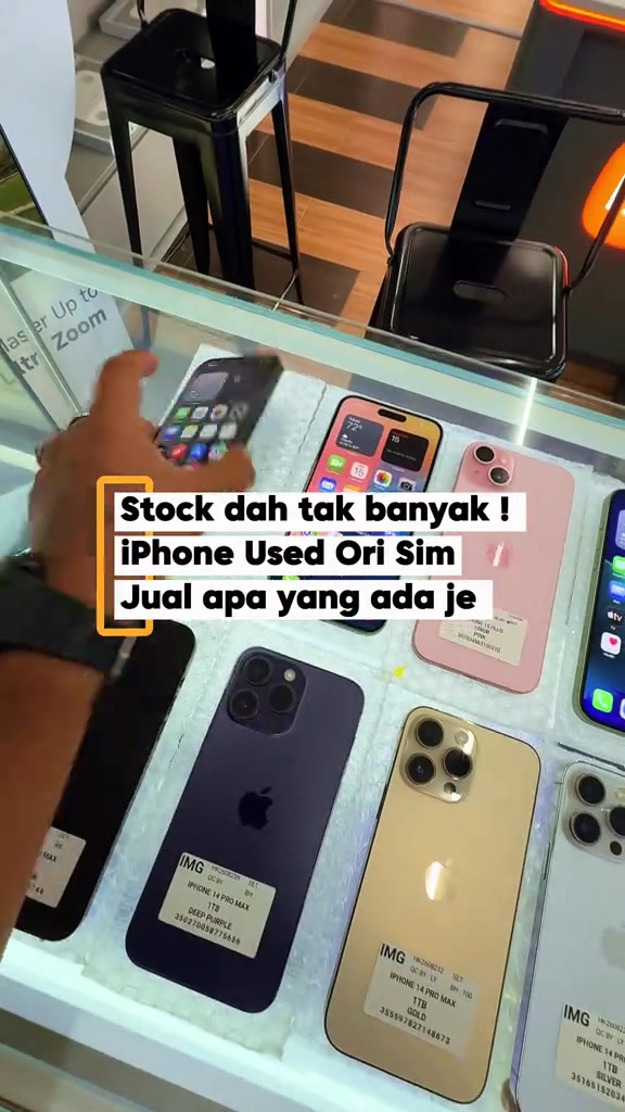 Cermin pameran kedai berisi iPhone terpakai, setiap unit ada label cetak model dan storage seperti iPhone 14 Pro Max 1TB Deep Purple dan Gold