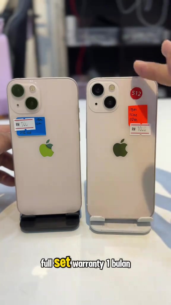Dua unit iPhone 13 warna pink di atas stand dengan pelekat harga RM900 dan RM1000 serta kapsyen full set warranty 1 bulan