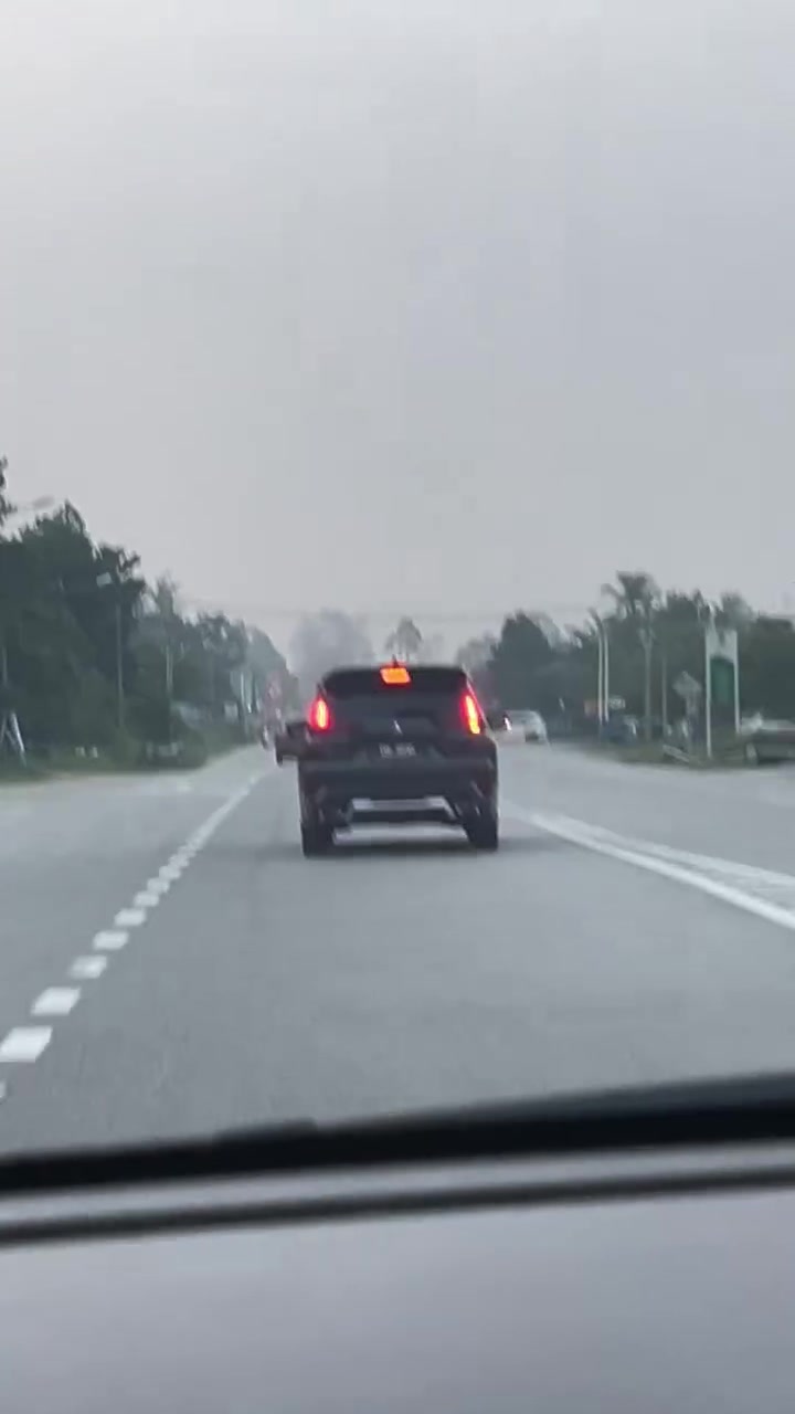 Pandangan dari dalam kereta ke jalan raya yang diselubungi jerebu kelabu, pokok di tepi jalan nampak samar