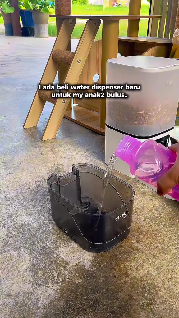 Tangan menuang air dari botol ke dalam tangki water fountain tanpa wayar yang diletak di lantai