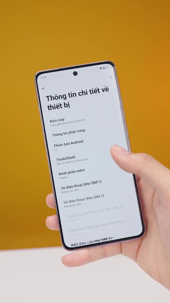 Màn hình cài đặt của điện thoại hiển thị dòng chữ moto g86 power 5G và phiên bản Android 15, cầm trên tay nền vàng