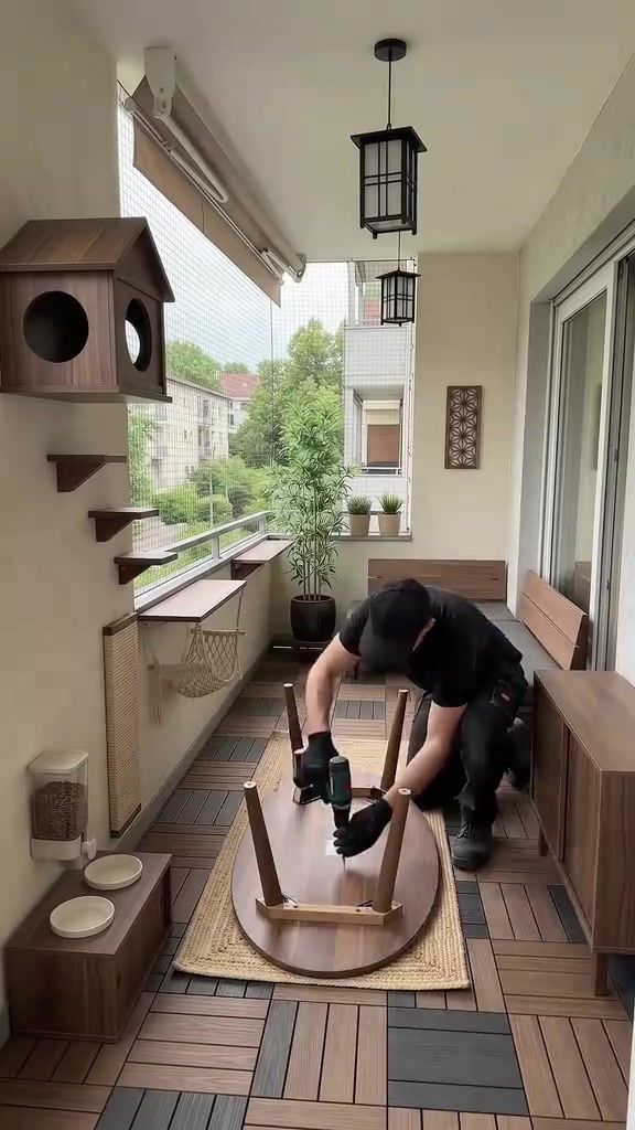 Balkoni apartment yang dipasang jaring dengan rumah kucing kayu di dinding, rak panjat, pokok pasu dan stesen makan kucing