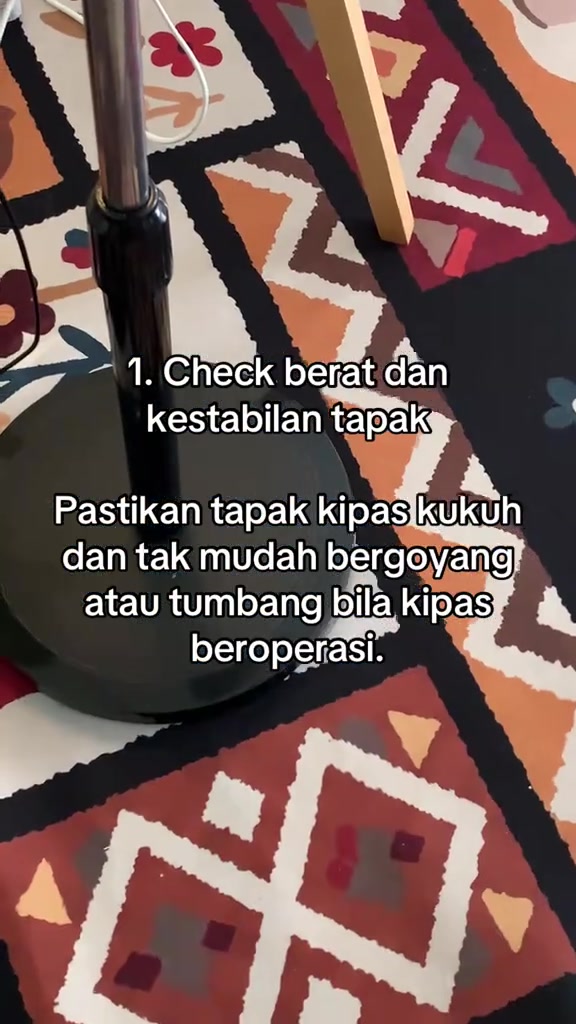 Tangan menekan tapak kipas stand fan hitam untuk uji kestabilan, dengan teks checklist nombor 1 tentang tapak