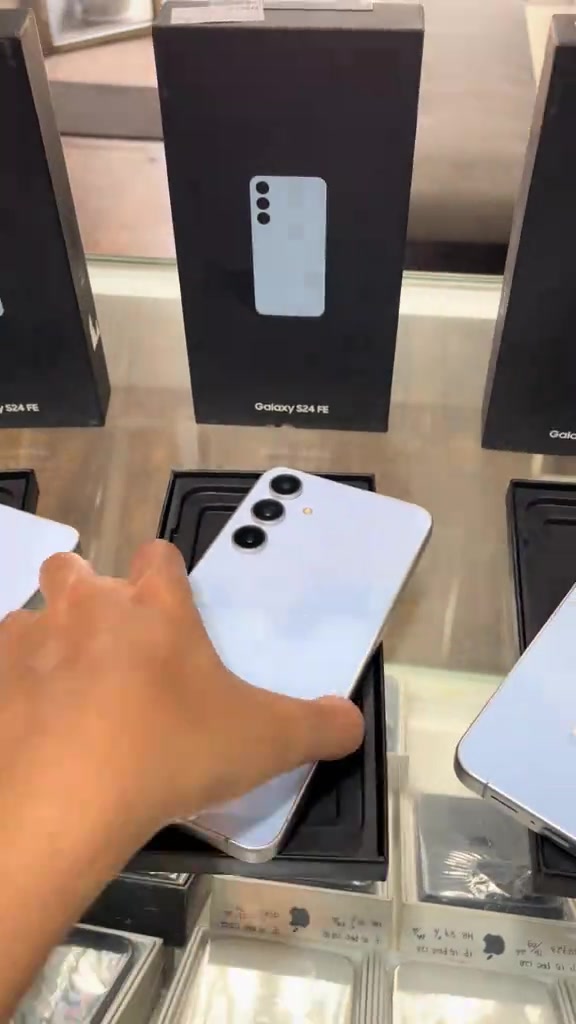 Tangan mengambil unit Samsung Galaxy S24 FE biru muda dari kotak dalam pameran kedai untuk diperiksa