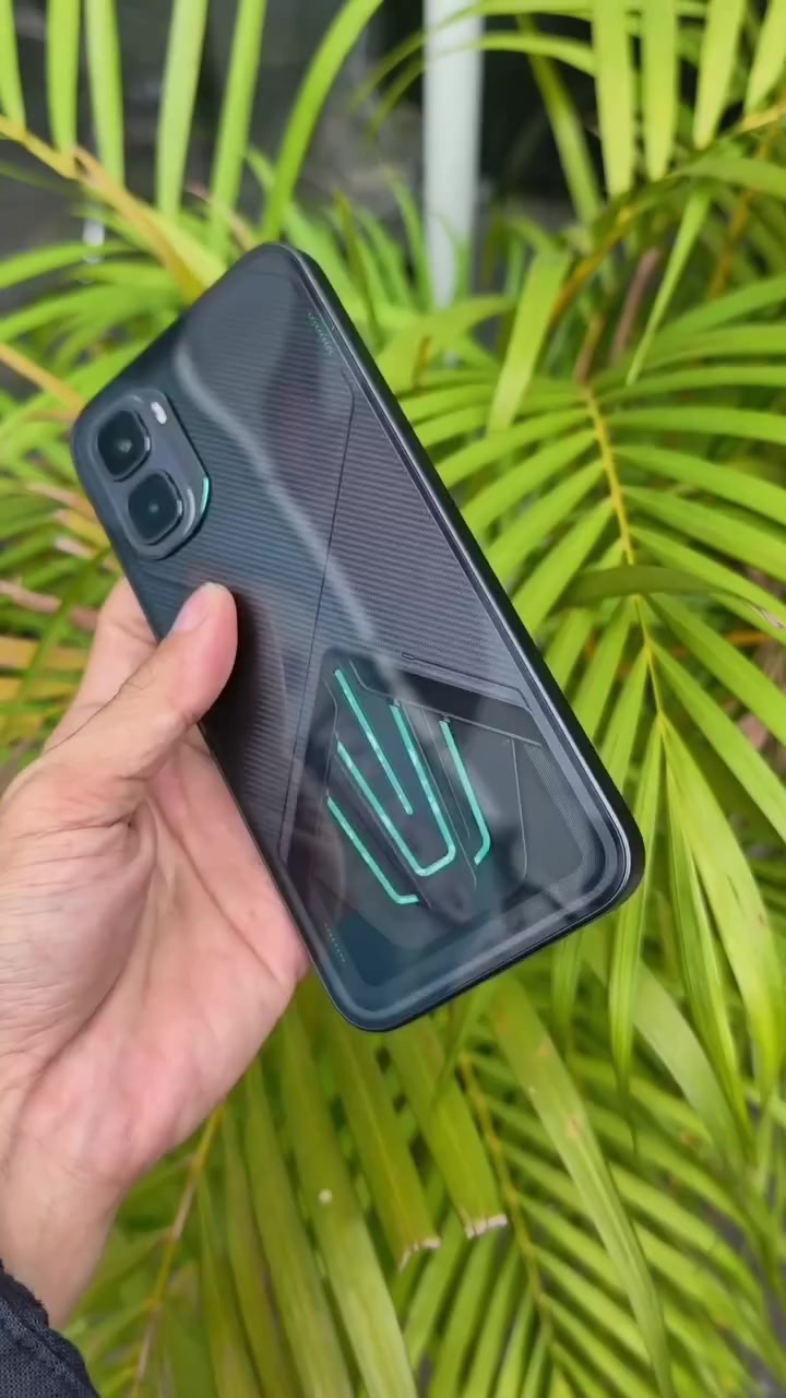Infinix GT 50 Pro warna hitam dilihat dari sudut condong menunjukkan modul penyejukan berlampu hijau, latar daun palma