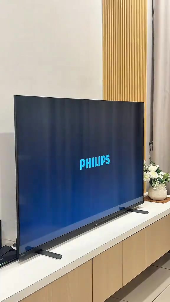TV skrin rata baharu diletakkan di atas konsol kayu di ruang tamu dengan logo Philips pada skrin