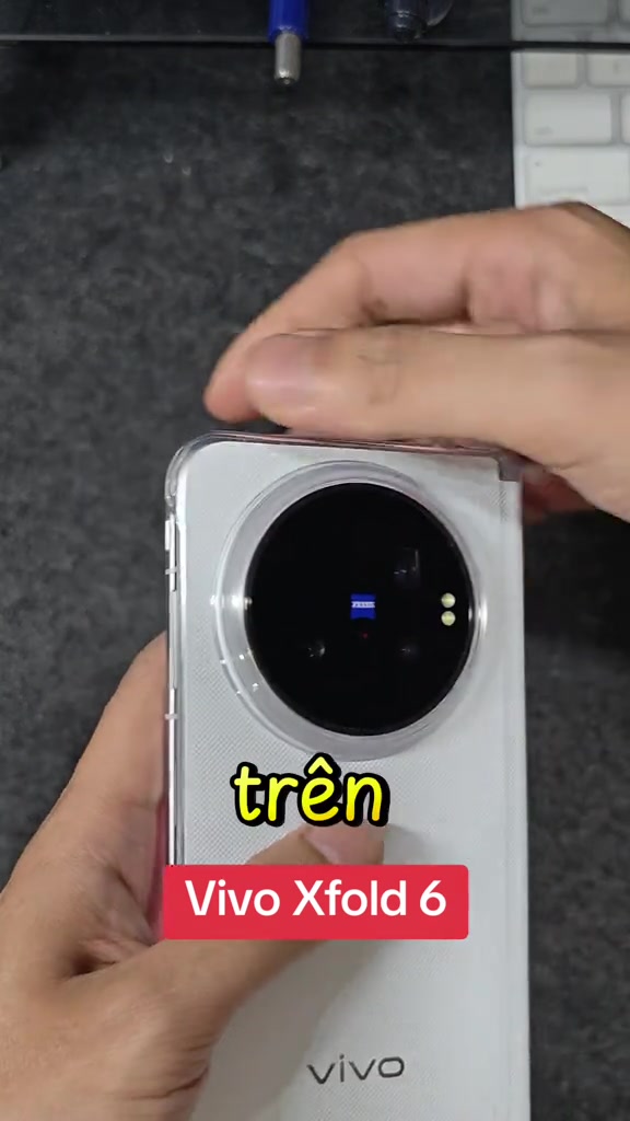 Cụm camera tròn màu đen có logo ZEISS trên mặt lưng màu trắng của vivo X Fold6, cầm trên tay