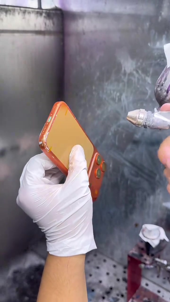 Kỹ thuật viên đeo găng tay trắng giữ bộ khung iPhone 17 Pro màu cam trong buồng sửa chữa