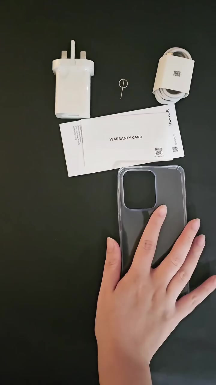 Kad waranti Honor bersama pengecas tiga pin, kabel USB, pin SIM dan sarung lutsinar disusun atas meja gelap