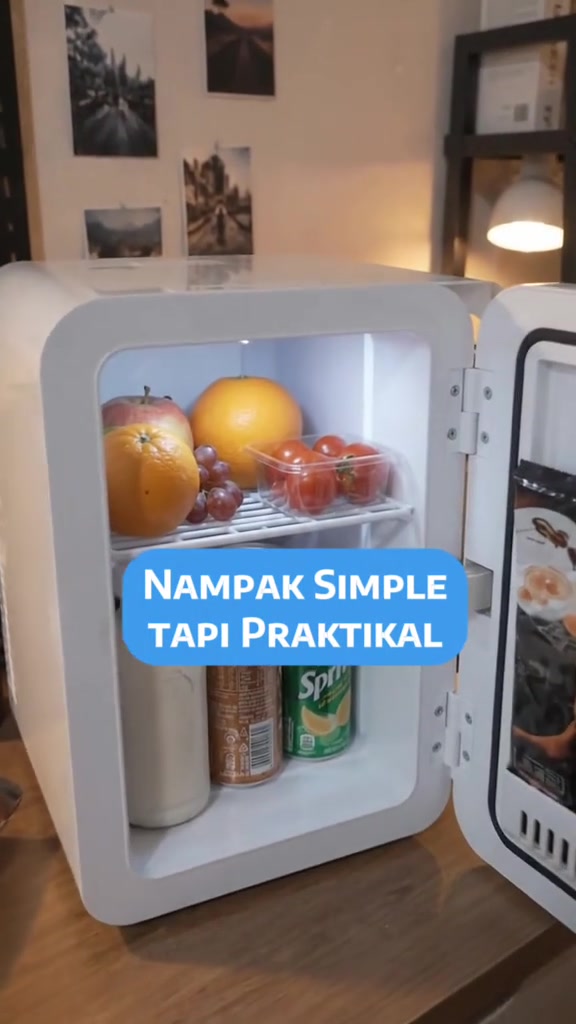 Peti sejuk mini putih terbuka di atas meja kayu berisi buah-buahan, tomato dalam bekas dan tin minuman