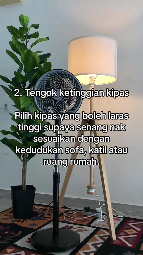 Kipas stand fan hitam jenis circulation berdiri di tepi lampu lantai dalam bilik, dengan teks checklist nombor 2 tentang ketinggian boleh laras