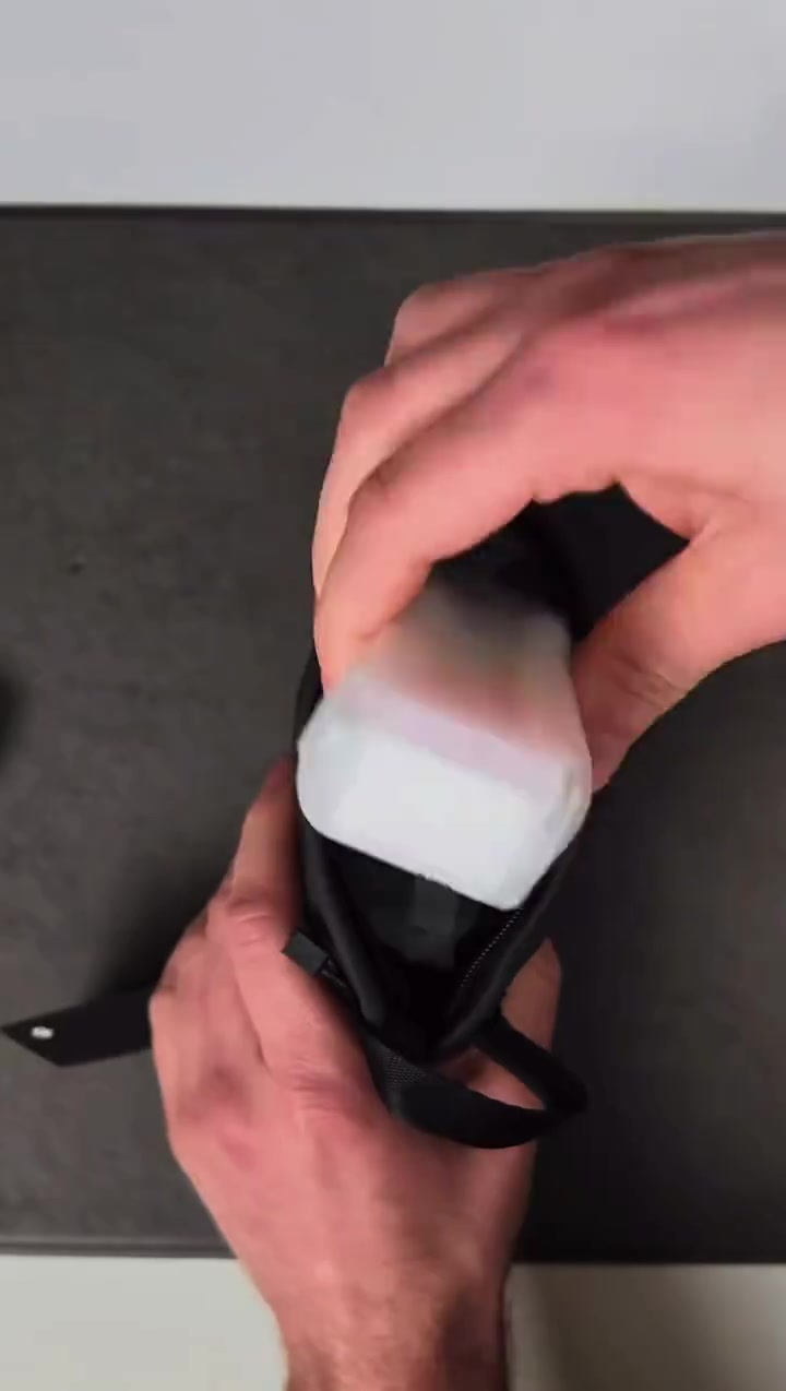 Tangan memasukkan bekas pengecas DJI Mic Mini 2S ke dalam pouch fabrik hitam daripada set rasmi