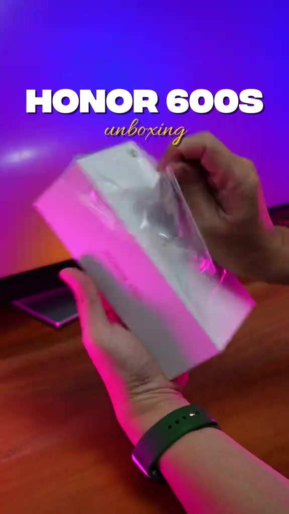 Kotak Honor 600S masih berbalut plastik sedang dibuka oleh dua tangan di atas meja