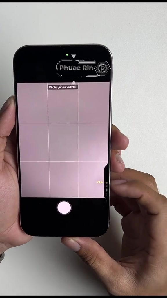 Một tay giữ iPhone, ngón trỏ đặt lên nút Camera Control cạnh phải khi màn hình đang mở ứng dụng camera