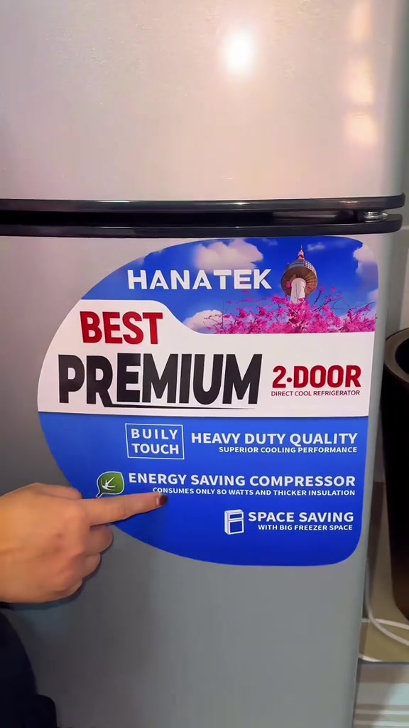 Pelekat pada badan peti sejuk Hanatek tertulis energy saving compressor consumes only 80 watts and thicker insulation, jari menunjuk pada pelekat