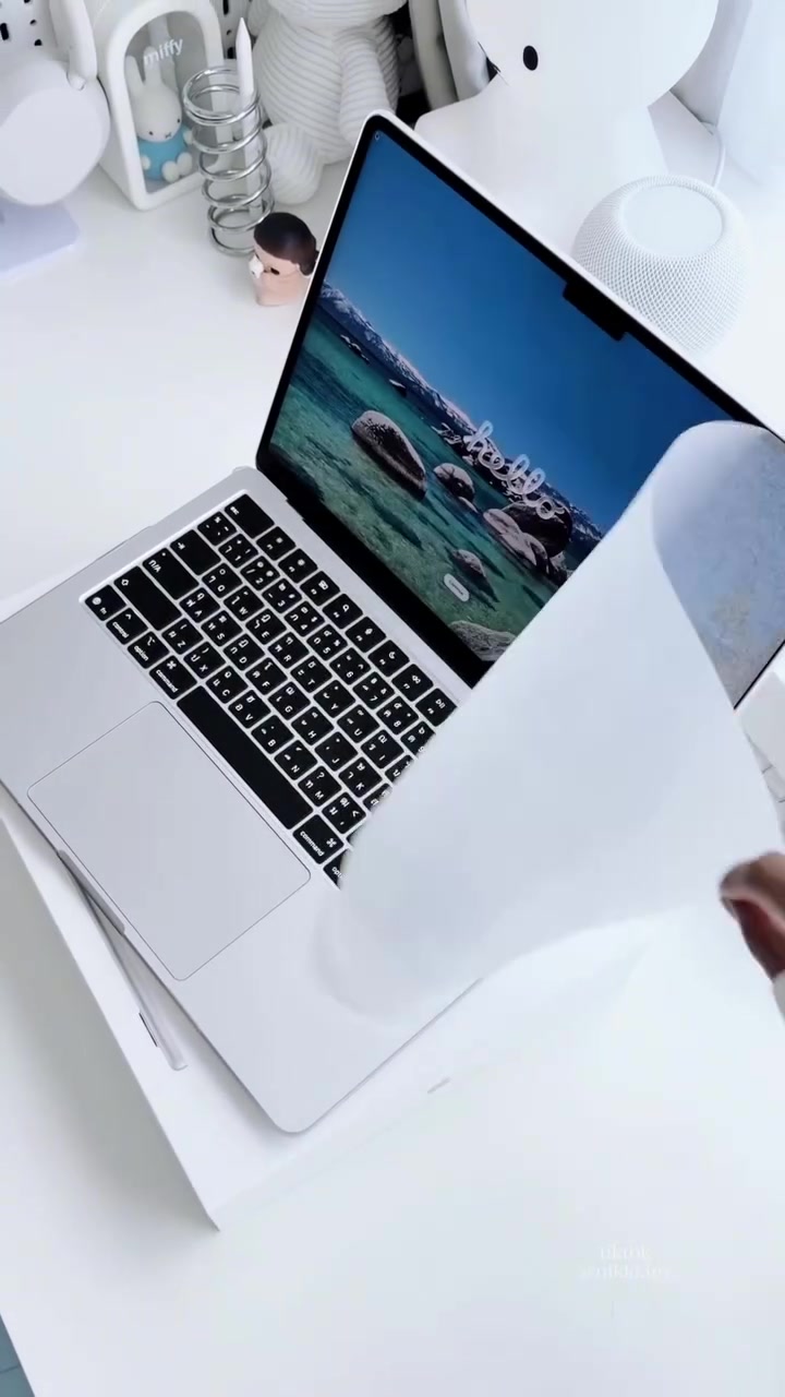 Tay đang bóc lớp giấy bảo vệ khỏi màn hình chiếc MacBook Air M5 màu bạc