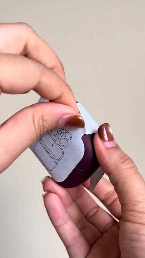 Tangan membuka balutan kertas pada kes pengecas Soundcore AeroClip 2 warna burgundy