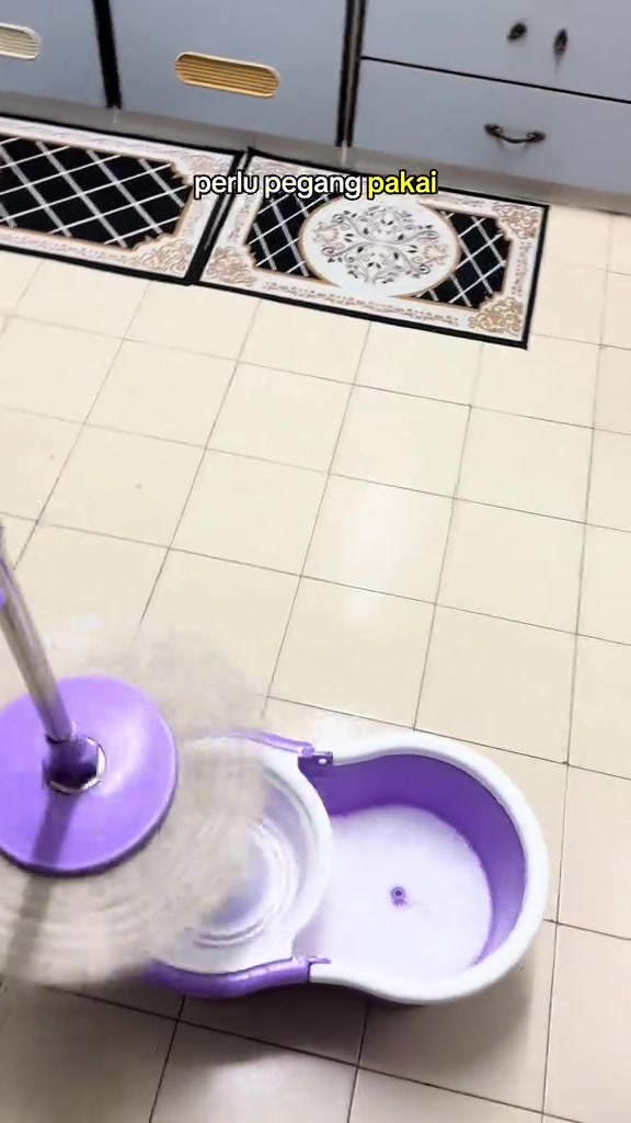 Kepala mop spin sedang dipusingkan di atas baldi spin berwarna ungu dan putih