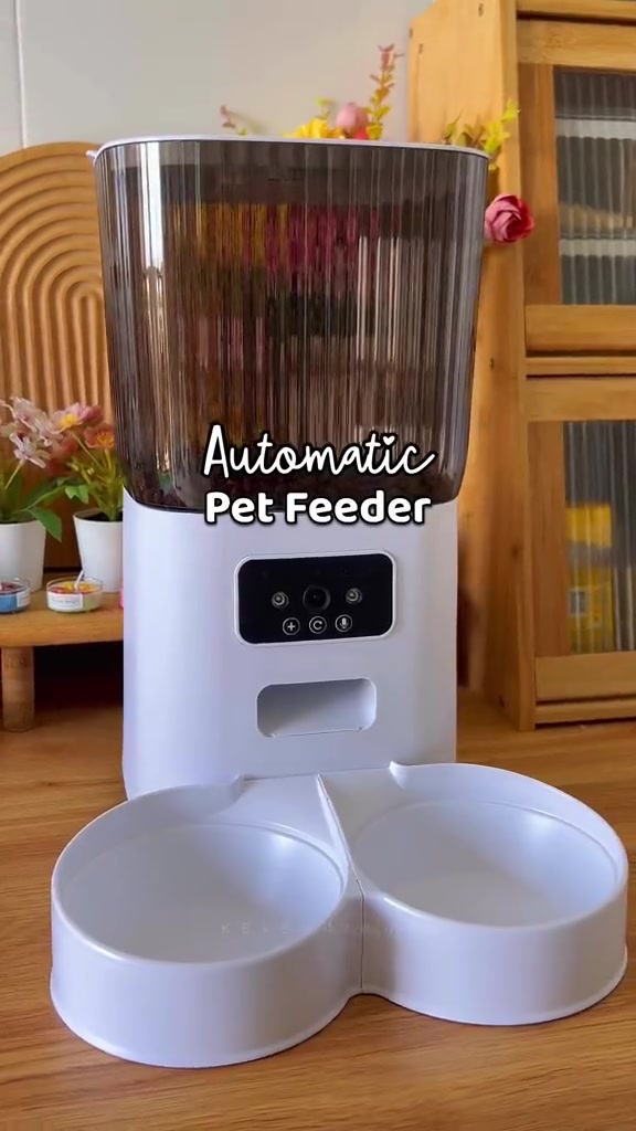Auto feeder putih dengan bekas atas gelap berpanel butang dan dua mangkuk berkembar di lantai kayu