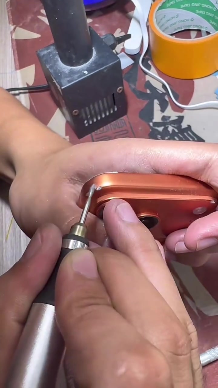 Hai bàn tay dùng tua vít thao tác ở góc khung iPhone 17 Pro màu cam trên bàn sửa chữa