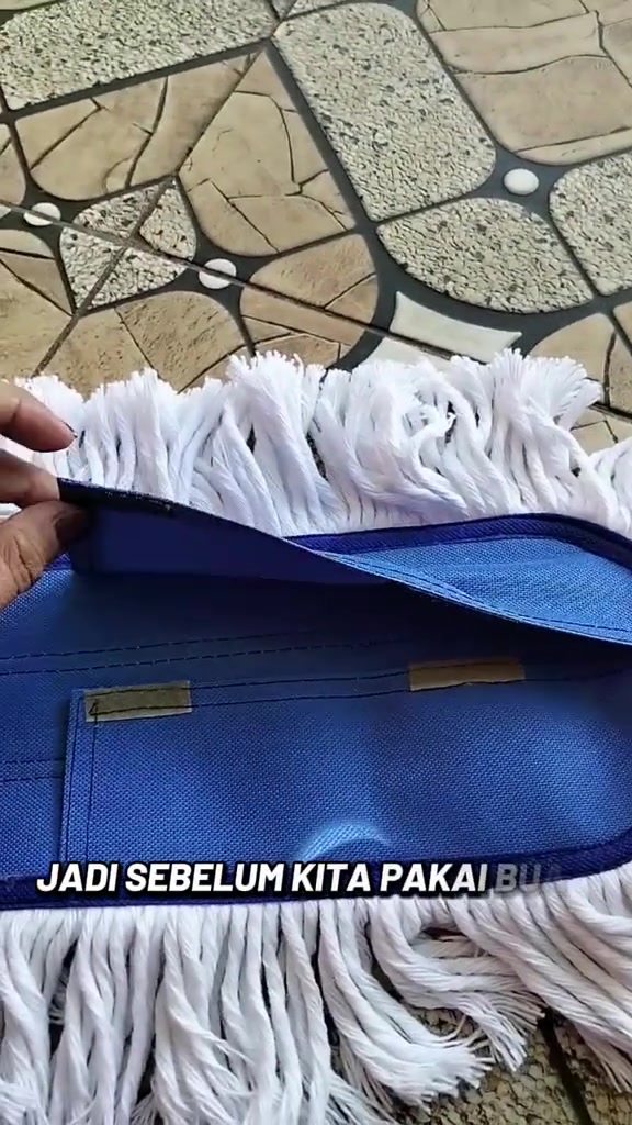 Tangan memegang refill kepala mop tali putih dengan tapak fabrik biru