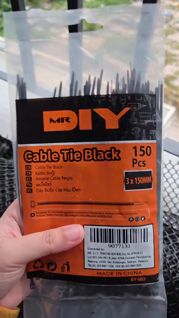 Peket cable tie hitam MR DIY dipegang dengan tangan, digunakan untuk mengikat jaring pada grill balkoni
