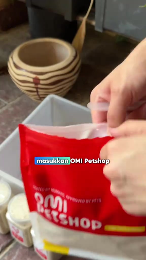 Tangan menuang kibbles dari beg merah ke bekas simpanan plastik