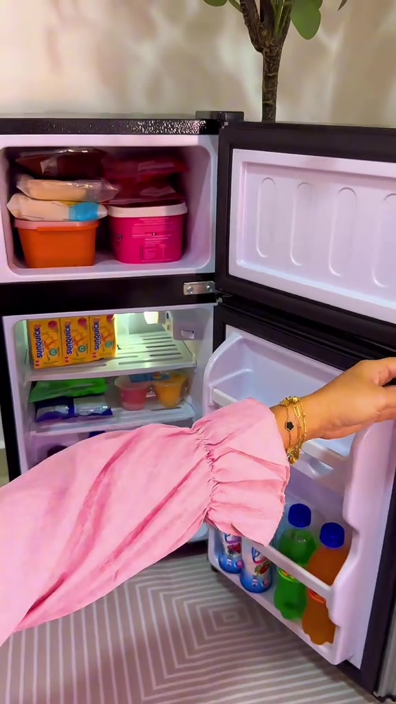 Peti sejuk mini dua pintu terbuka penuh: ruang freezer atas berisi bekas makanan bertutup, ruang bawah berisi kotak minuman dan rak pintu berisi botol