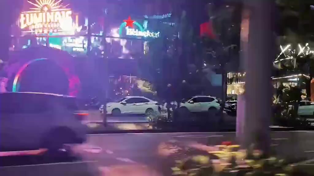 Phố đêm với biển hiệu neon và dòng xe chạy qua trong MV cộng đồng