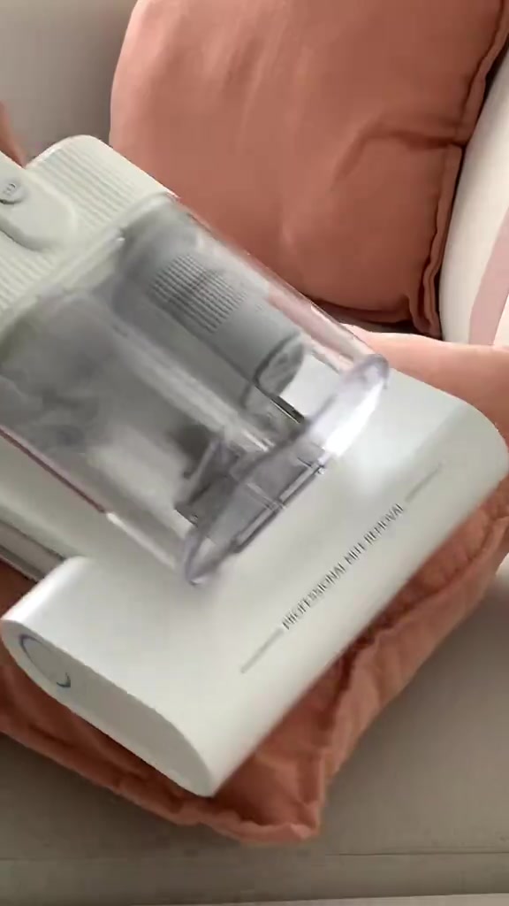 Dust mite vacuum warna putih dengan cup habuk telus sedang digunakan atas kusyen warna peach