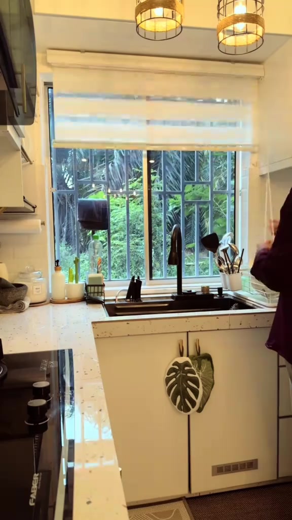 Zebra blind putih separuh naik pada tingkap dapur bergrill luar dengan kabinet di kiri kanan sinki