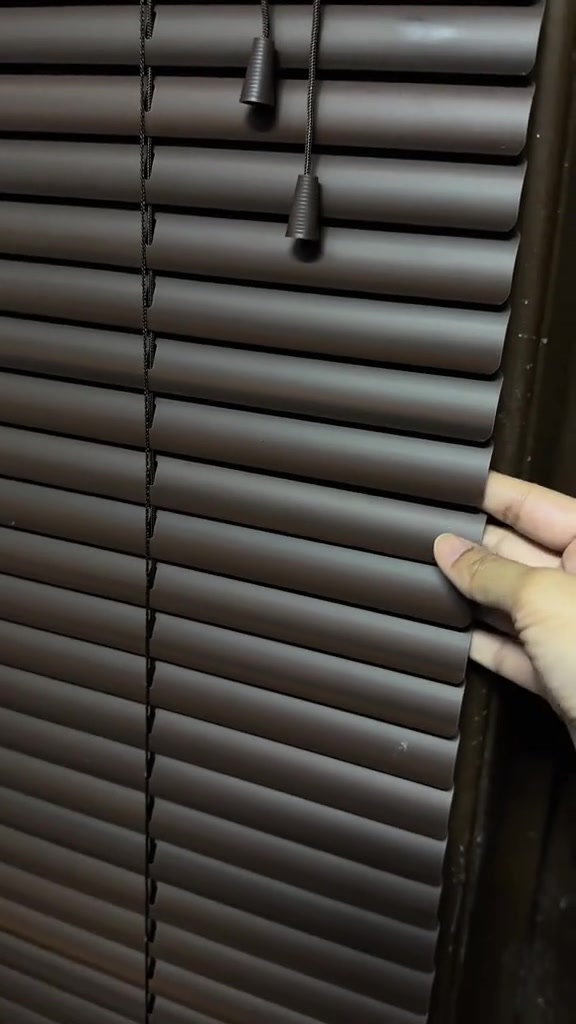 Tangan menyentuh slat bidai venetian aluminium warna coklat dengan tali tarik tergantung