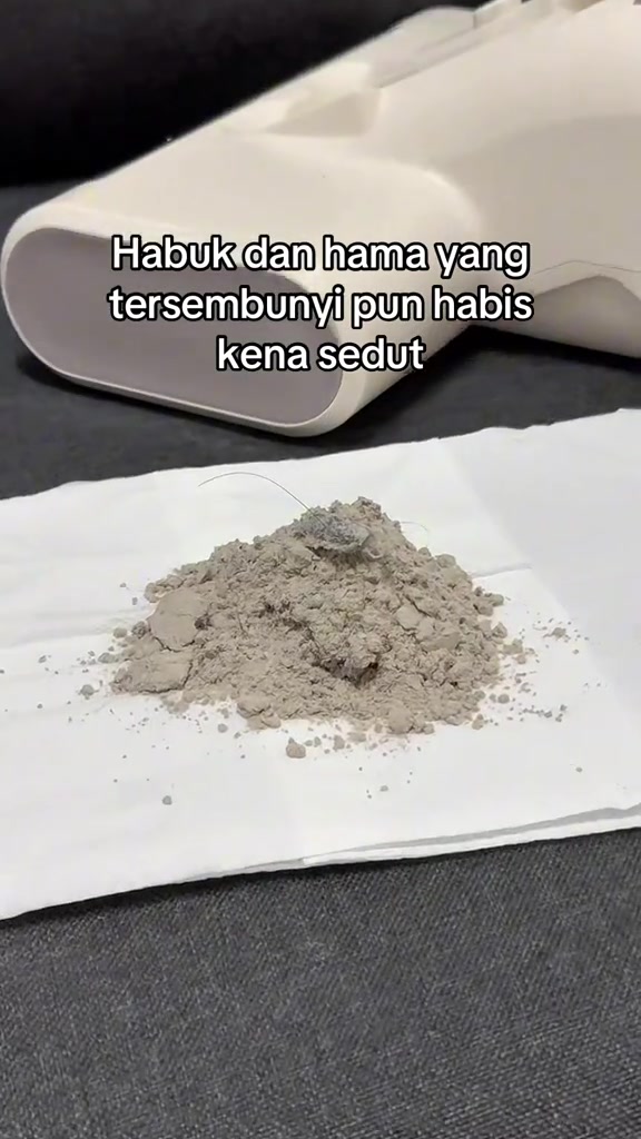 Longgokan habuk halus warna kelabu atas tisu putih selepas tilam divacuum, dengan badan dust mite vacuum di latar belakang