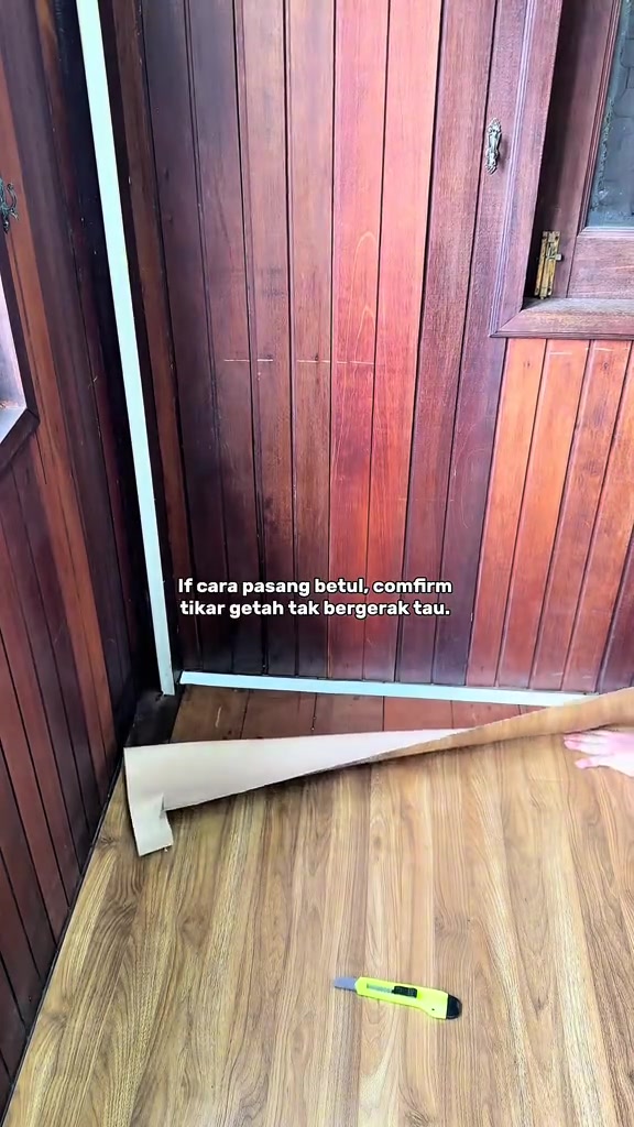 Tepi hamparan tikar getah corak kayu di hadapan pintu kayu, dengan pisau cutter terbaring di atas lantai