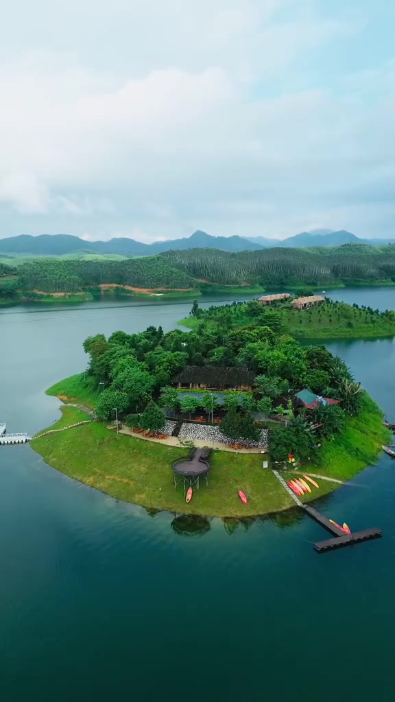 Đảo nhỏ phủ cây xanh với vài nếp nhà và thuyền kayak giữa mặt hồ nước xanh ngọc, nhìn từ trên cao